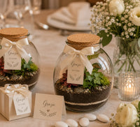 Terrarium Carlotte utilizzato come bomboniera green per matrimonio con confezione regalo, fiocco panna, decorazioni floreali e allestimento elegante.