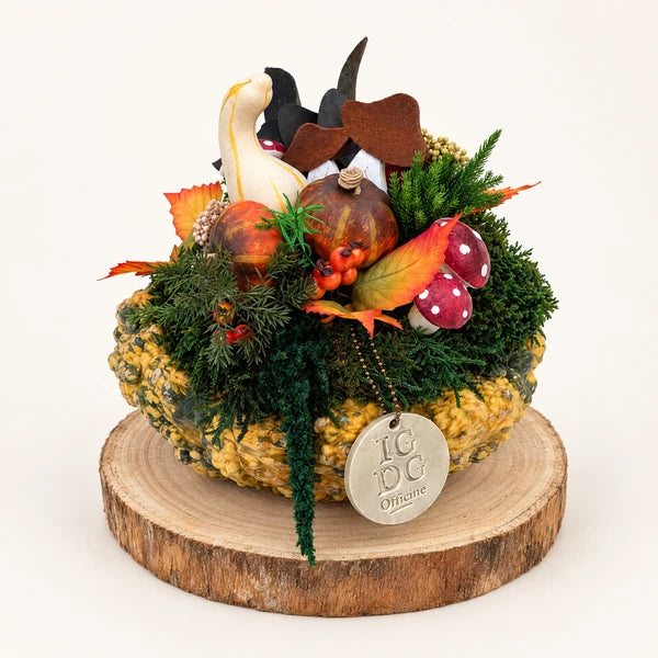 Centrotavola autunnale con zucche decorative, funghi rossi e fogliame verde su base in legno, su sfondo neutro.