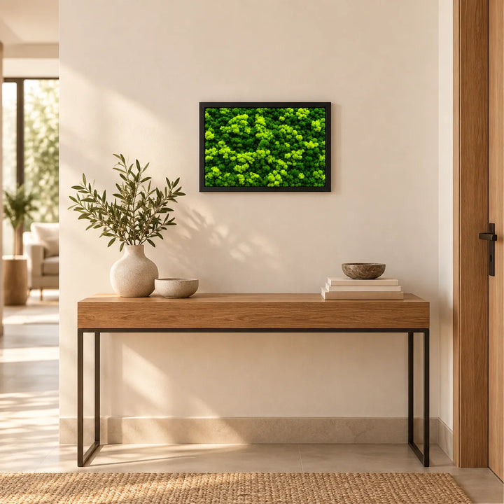 Quadro di licheni stabilizzati con cornice nera appeso sopra una consolle in legno all'ingresso, arredo con verde stabilizzato