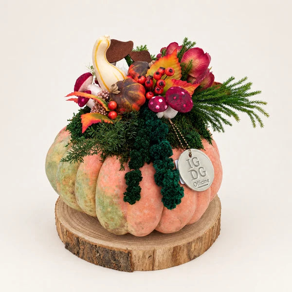 Zucca vera con verde stabilizzato e decorazioni autunnali, su base tonda in legno inclusa, fotografata su sfondo neutro.