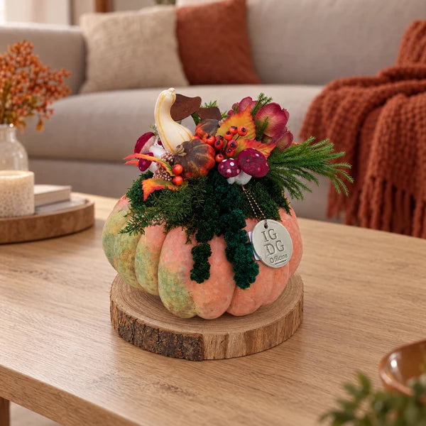 Composizione in zucca vera con verde stabilizzato e decorazioni autunnali, su base in legno, sopra un tavolino in soggiorno.