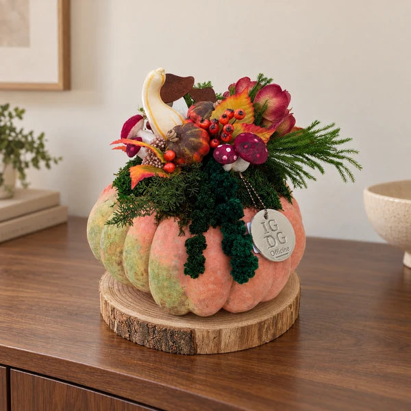 Zucca vera con verde stabilizzato ricadente e decorazioni autunnali, completa di base tonda in legno, esposta su una credenza.